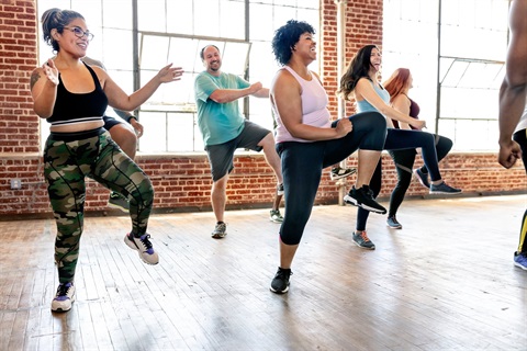 Five people, four women and one man, dressed in active wear participating in a fitness class, smiling and enjoying themselves.