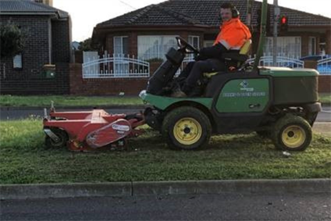Maintenance staff on drivable lawn mower tending to a centre medium