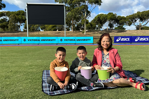 Councillor Lam with two young twin boys at Skinner Reserve in front of scoreboard screen for the movie night