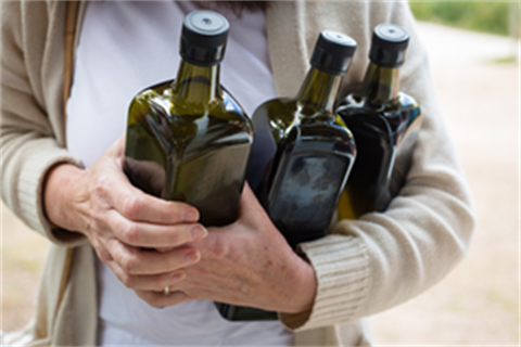 An image of a person holding three bottles of olive oil against their chest