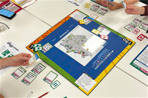 A board game on a table with several hands holding cards