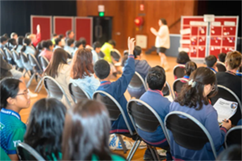A group of students sitting in an auditorium with one student having their hand up